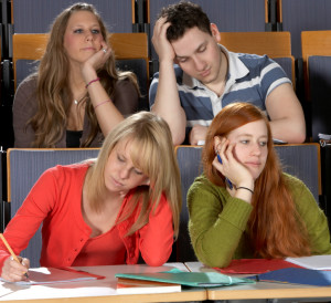 Photo of four students sitting in a classroom, all in postures of boredom.